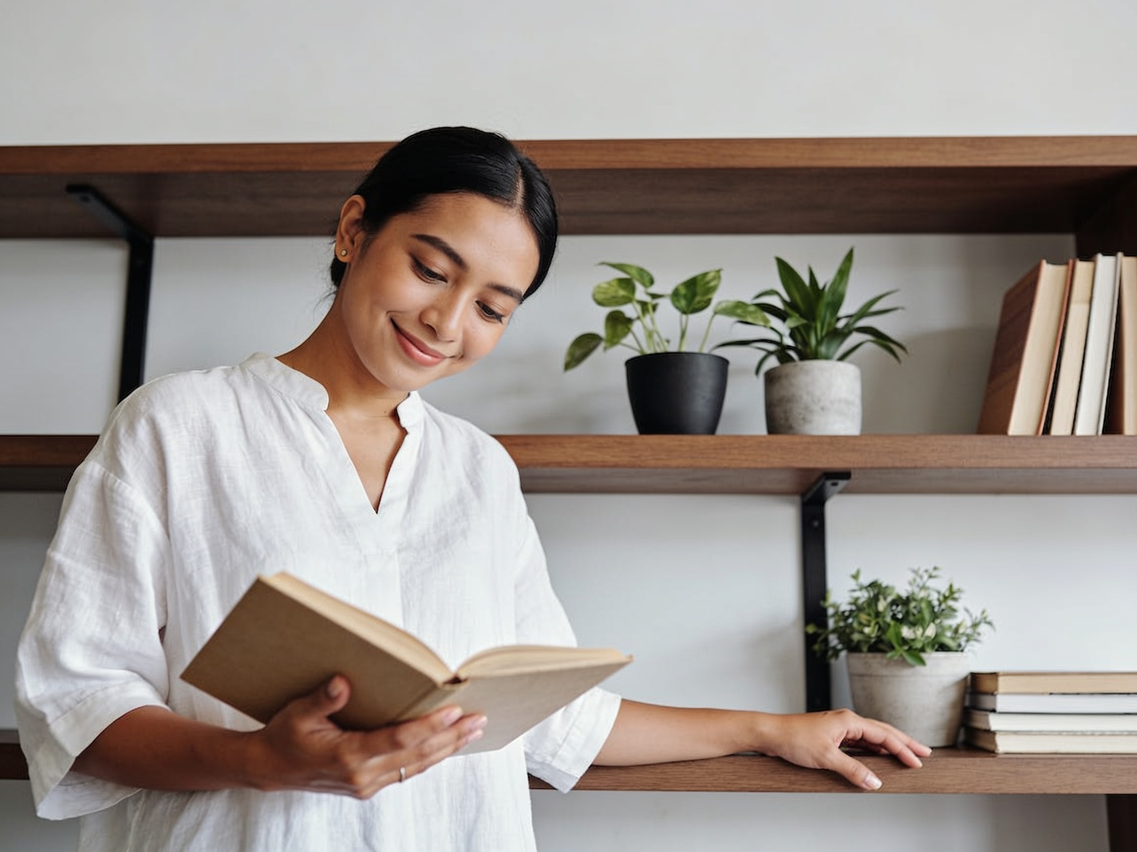 Wanita Indonesia memeriksa rak buku kayu untuk merasakan dampak gaya hidup minimalis yang tenang.